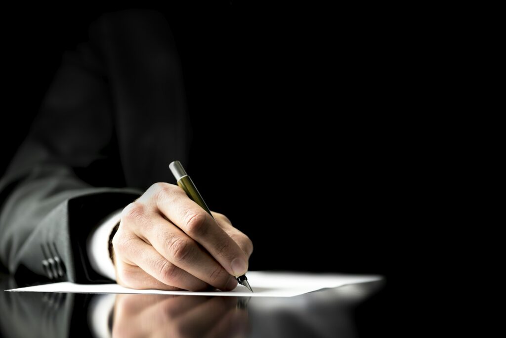 Close-up of a businessperson's hand signing a document, symbolizing the finalization of a dental practice purchase.